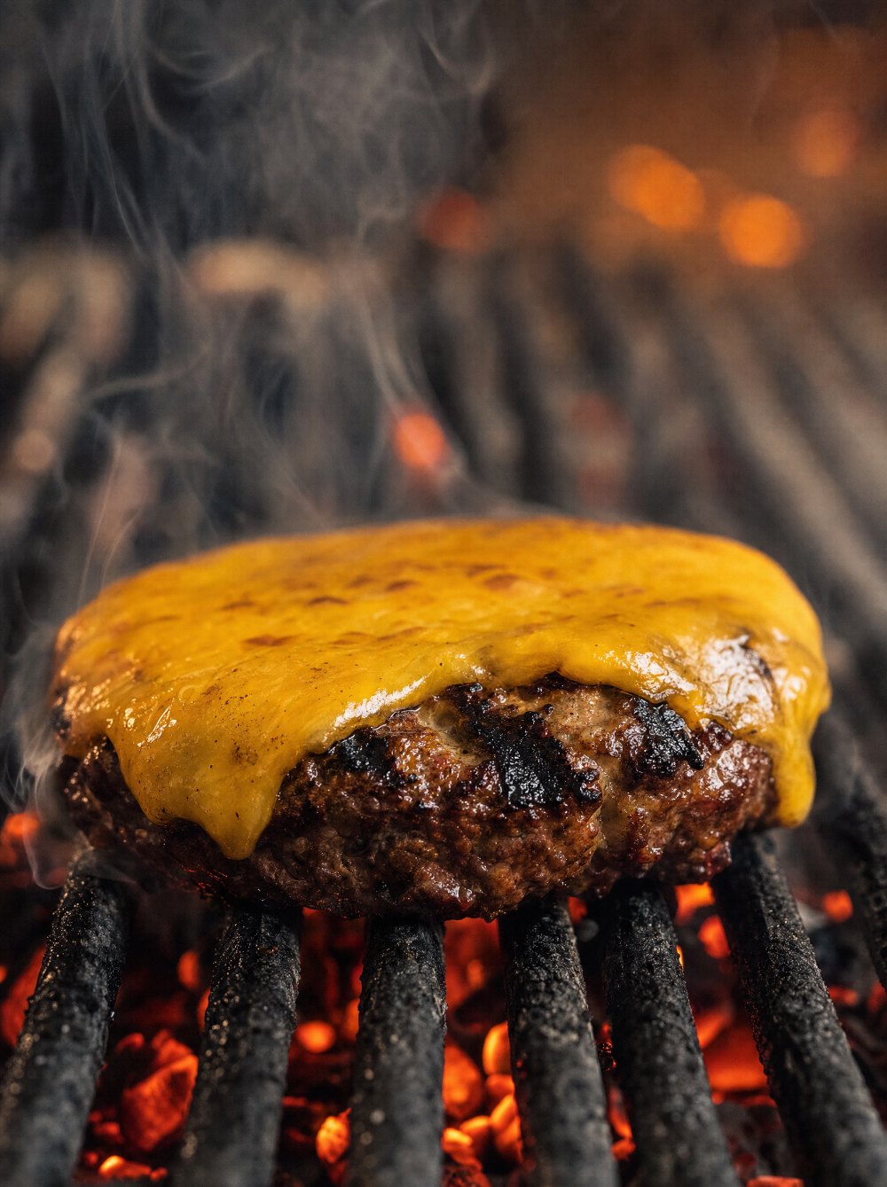 O hambúrguer virado na grelha, com marcas de brasa e uma fatia de cheddar derretendo por cima